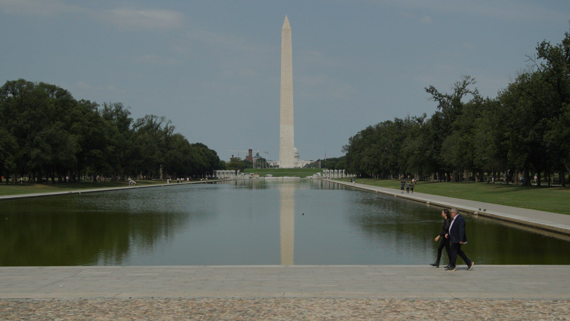 David M. Luna and Sam Rad walking beside the Reflecting Pool, the Washington Monument ahead